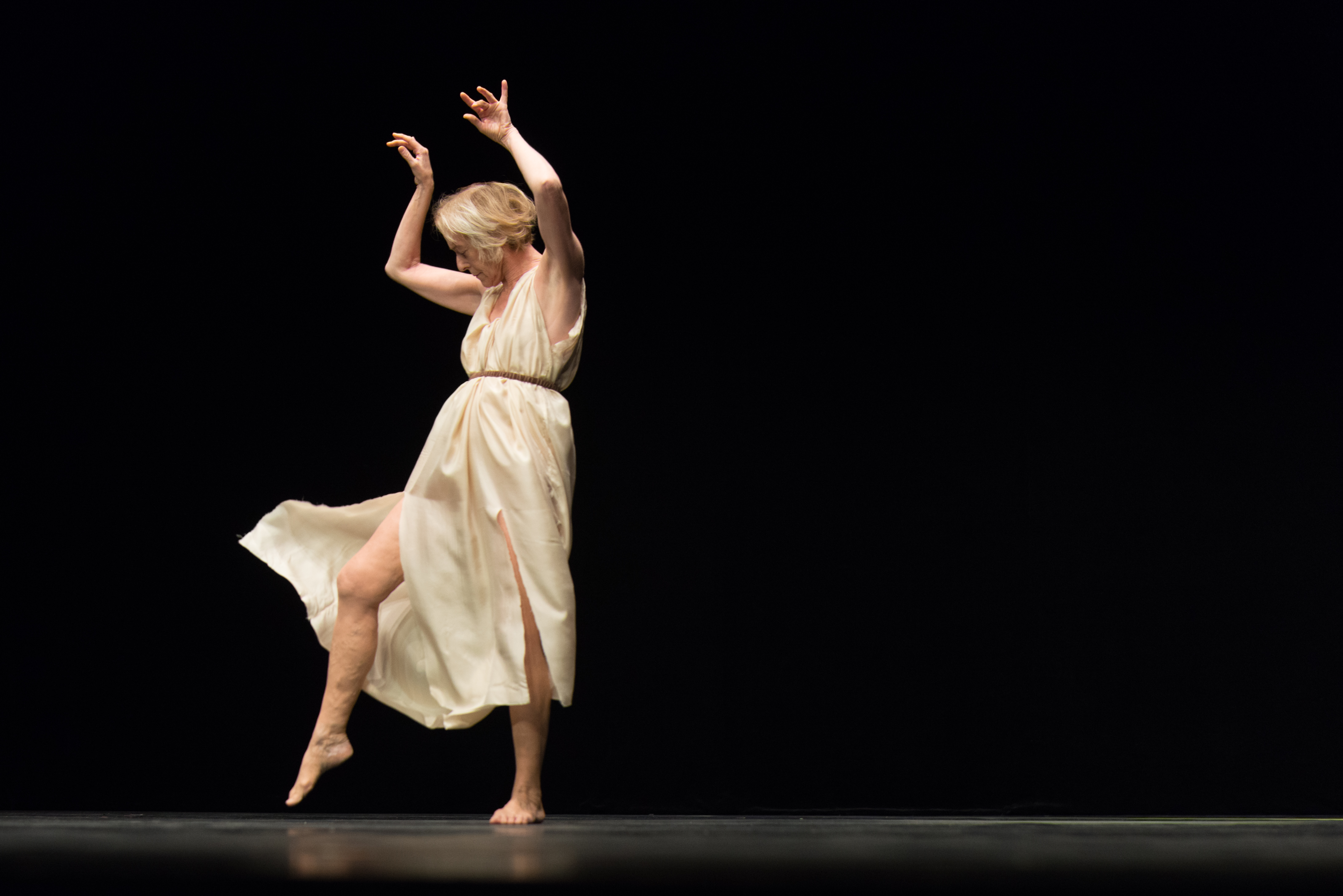 Die 70-jährige Tänzerin Elizabeth Schwartz als Isadora Duncan in graziler Pose in einem weißen klassizistischen Kleid