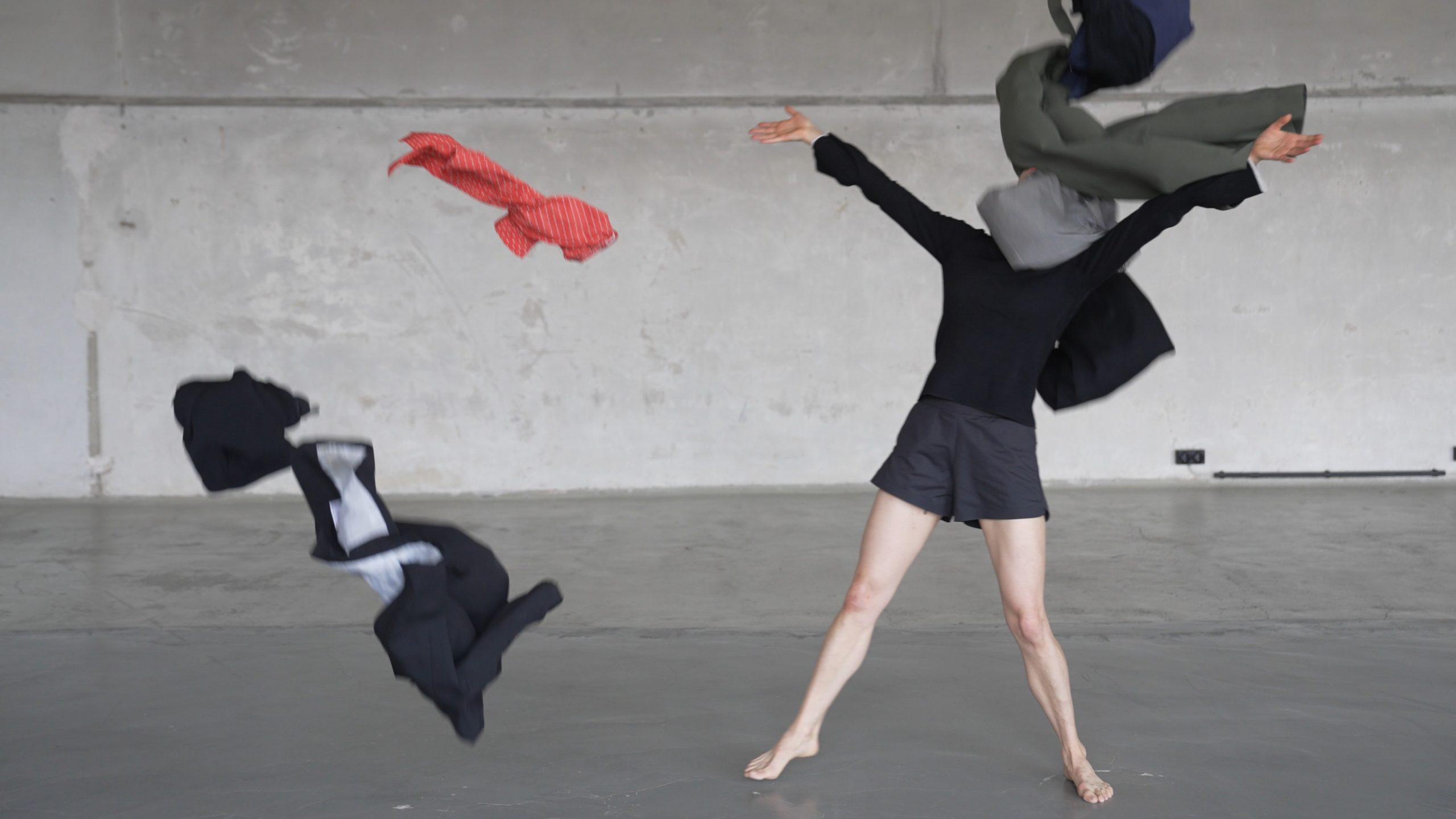 Tanz vom Tod | Das letzte Plötzlich | Maria Walser © Nora Wetzel. Eine Frau in einem schwarzen kurzen Kleid mit nackten Beinen steht breitbeinig auf der Bühne. Ihr Kopf ist von einem grauen Stoff verdeckt und zwei Kleidungsstücke fliegen durch die Luft.